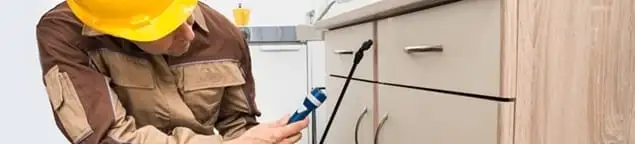 Roach exterminator applying treatment under kitchen cabinets in Birmingham, AL
