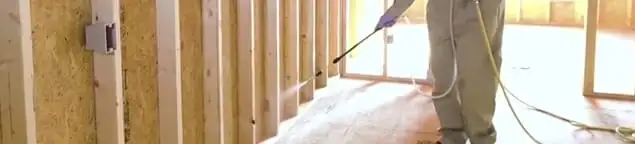 Termite treatment technician applying spray along framing and unfinished walls in Birmingham, AL